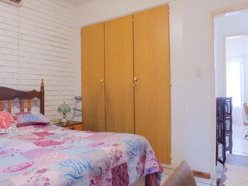 A bedroom featuring built-in wooden cupboards, an exposed brick feature wall, and an integrated air conditioning unit.