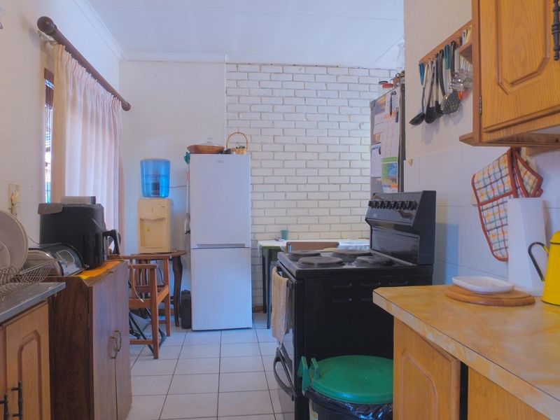A functional kitchen featuring wooden cabinetry, tiled flooring, an exposed brick feature wall, and a freestanding stove with a tiled backsplash.