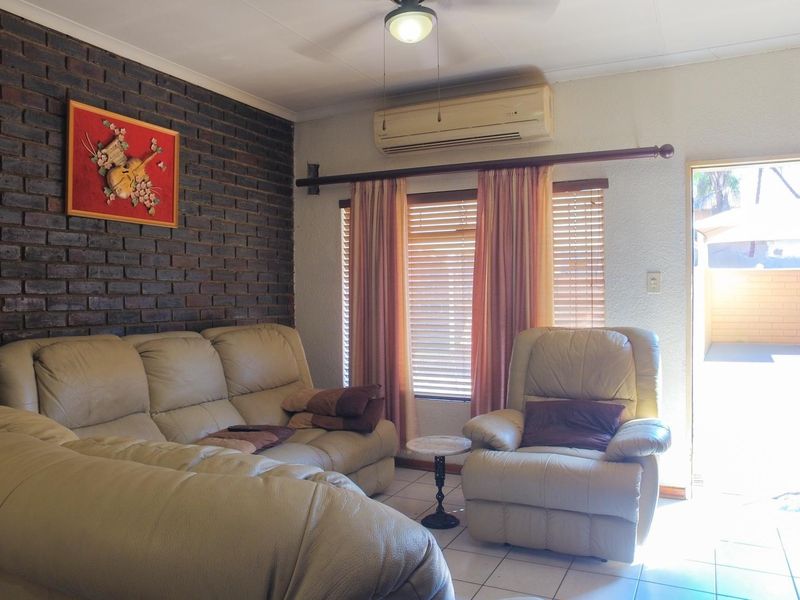 Living room featuring an exposed brick feature wall, tiled flooring, ceiling fan, and a wall-mounted air conditioning unit with direct access to the exterior.