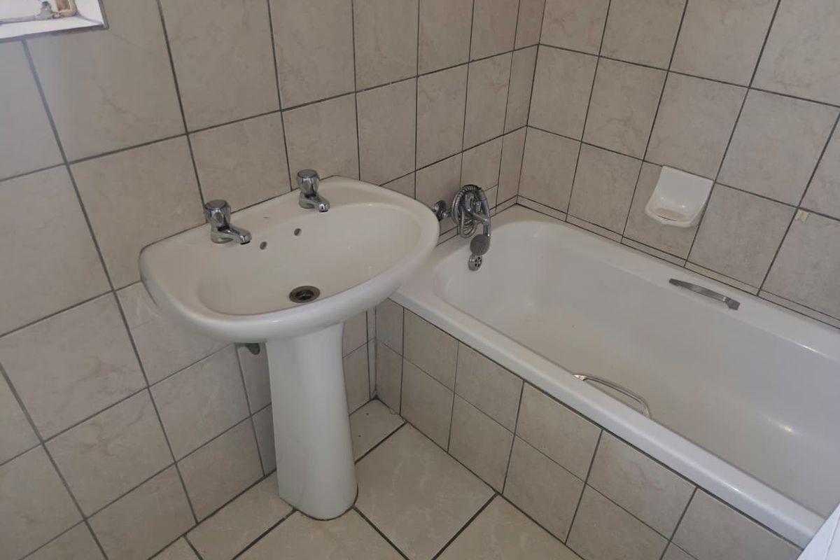 A functional bathroom featuring a pedestal basin, bathtub, and neutral wall and floor tiling, offering a blank canvas for potential modernization.
