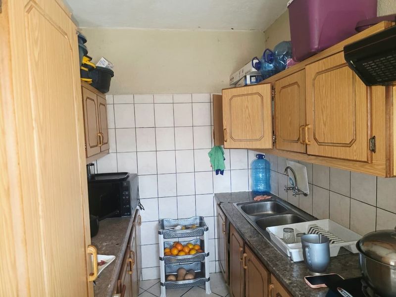 A compact kitchen featuring dated laminate cabinetry, a double bowl sink with mixer tap, and tiled splashbacks, offering potential for a modern renovation.