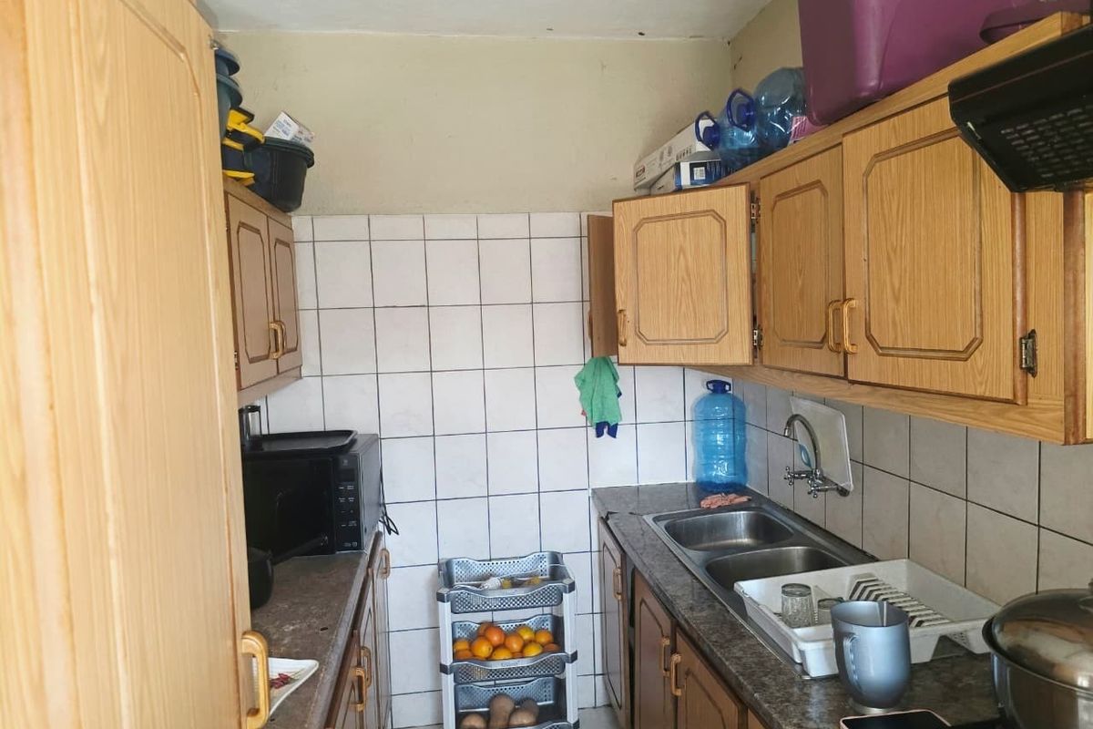 A compact kitchen featuring dated laminate cabinetry, a double bowl sink with mixer tap, and tiled splashbacks, offering potential for a modern renovation.