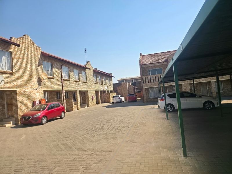 Exterior view of a townhouse complex featuring face brick facades, a paved driveway, and covered carport parking.