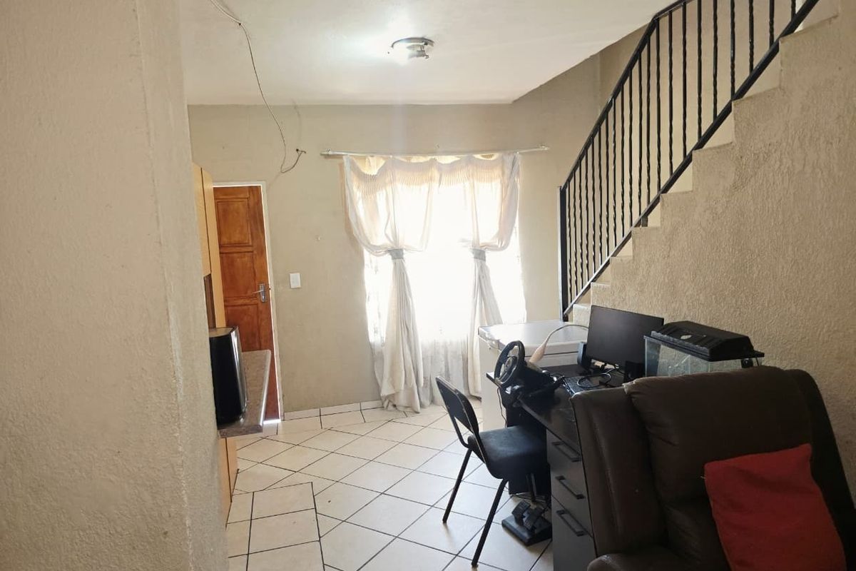 Open-plan living area featuring tiled flooring and a staircase with a metal balustrade, requiring cosmetic updates to improve the overall finish.