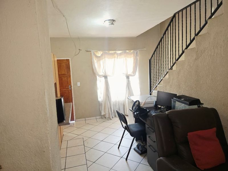Open-plan living area featuring tiled flooring and a staircase with a metal balustrade, requiring cosmetic updates to improve the overall finish.