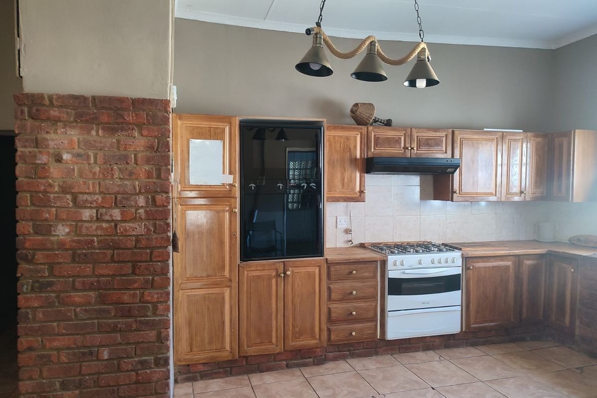 A rustic kitchen featuring wooden cabinetry, a gas stove with extractor fan, built-in oven, and an exposed brick feature pillar.