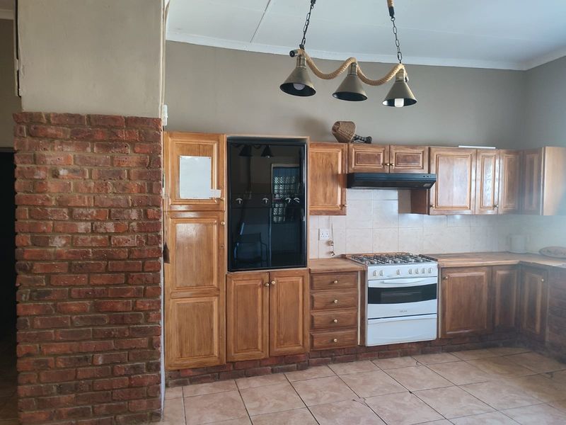 A rustic kitchen featuring wooden cabinetry, a gas stove with extractor fan, built-in oven, and an exposed brick feature pillar.