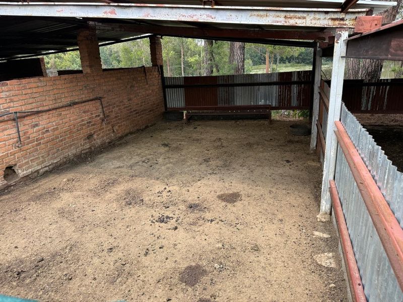 A rustic, open-sided utility structure or animal shelter featuring exposed brickwork, corrugated iron roofing, and metal cladding, showing significant signs of weathering.