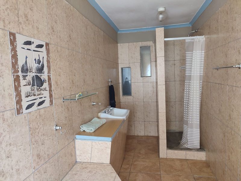 A functional bathroom featuring a walk-in shower, tiled walls and flooring, and a built-in vanity basin with storage counter.