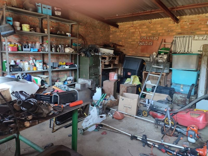 A functional utility or workshop space featuring exposed brick walls and corrugated metal roofing, currently utilized for storage and equipment maintenance.
