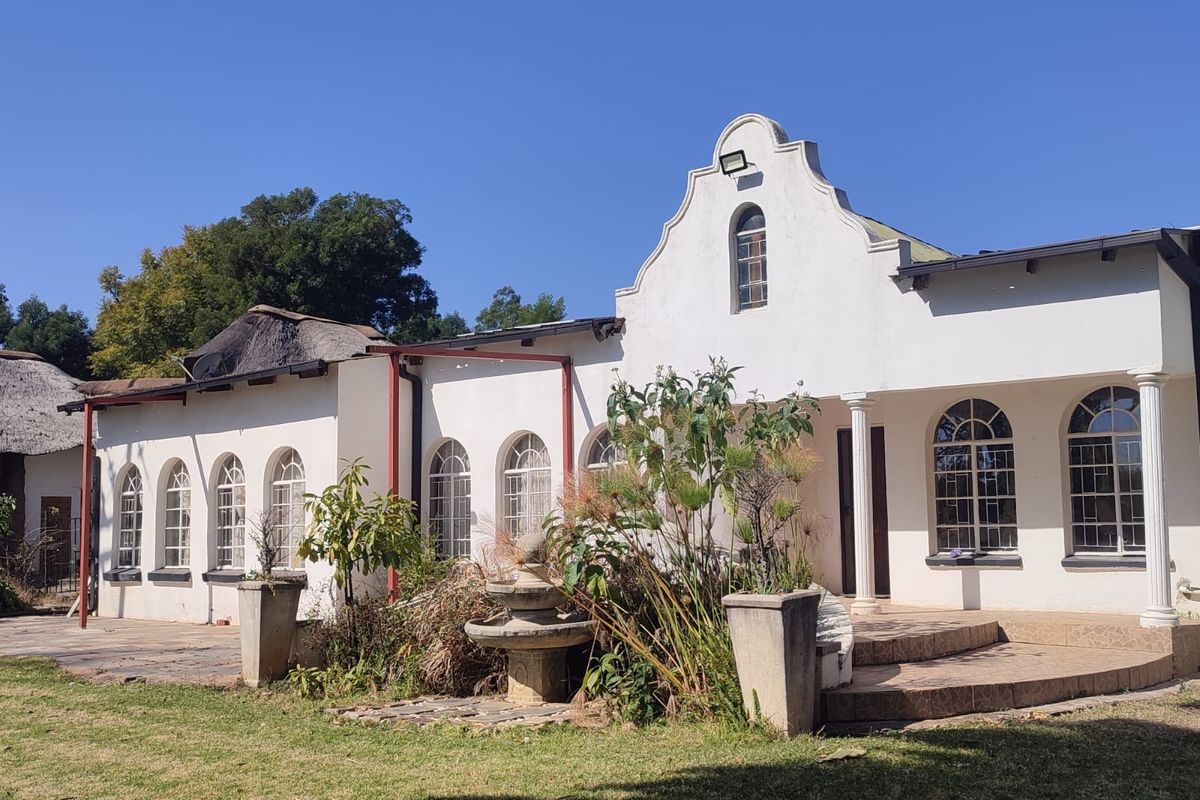Rear elevation of a farm-style residence featuring arched windows, a gabled facade, and a tiled patio area with a central stone fountain.