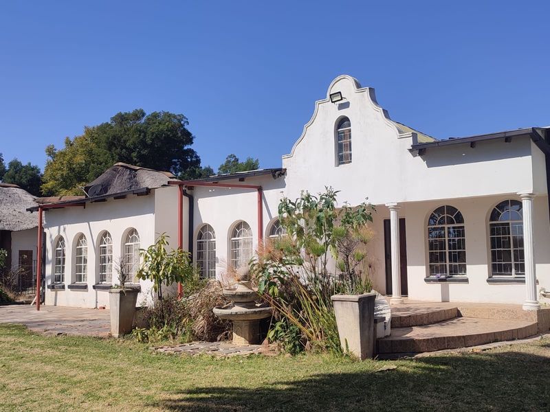 Rear elevation of a farm-style residence featuring arched windows, a gabled facade, and a tiled patio area with a central stone fountain.