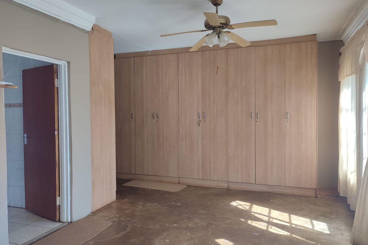 A spacious bedroom featuring extensive built-in wooden cupboards, a ceiling fan, and direct access to an adjoining room.
