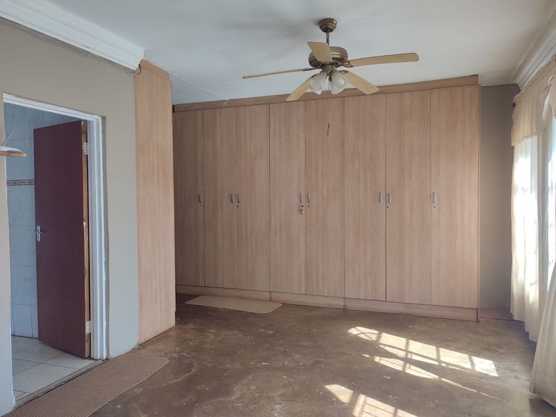 A spacious bedroom featuring extensive built-in wooden cupboards, a ceiling fan, and direct access to an adjoining room.