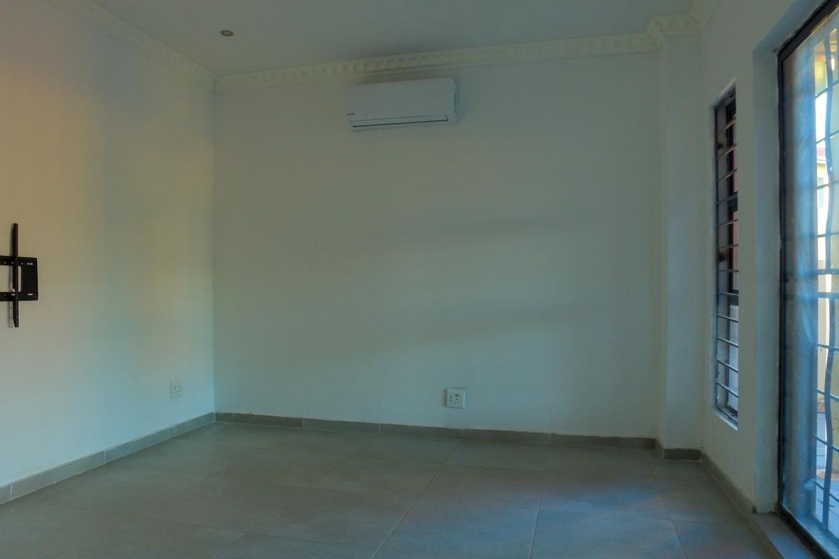 An empty living room featuring tiled floors, a wall-mounted air conditioning unit, and a sliding glass door with security bars.