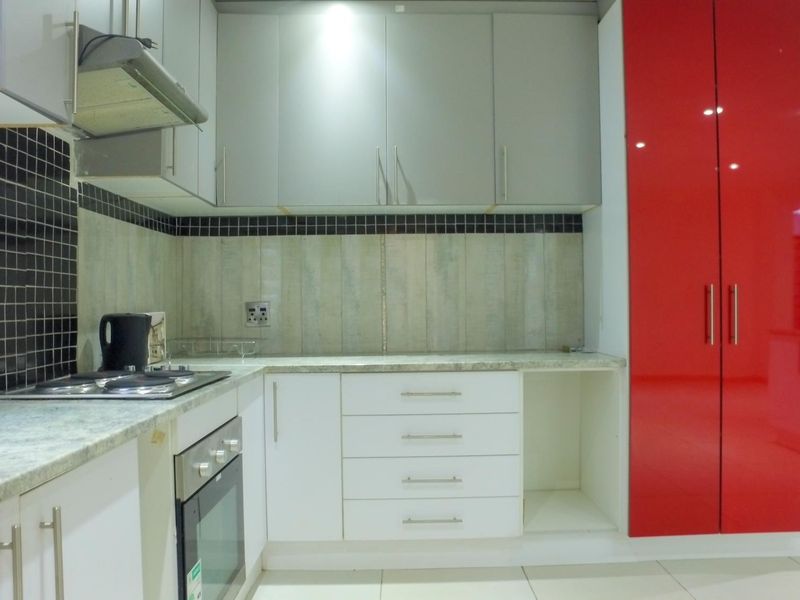 Modern kitchen featuring white and red cabinetry, stone countertops, built-in oven, gas hob, and a stylish tiled backsplash.