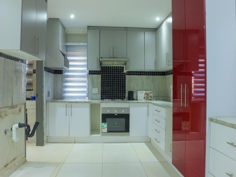 Modern kitchen featuring high-gloss cabinetry, built-in oven, extractor fan, and stone countertops, currently awaiting final plumbing installation.