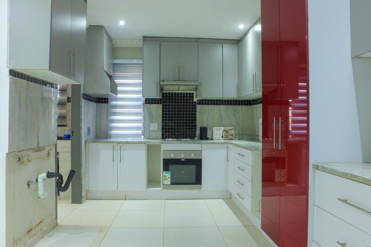 Modern kitchen featuring high-gloss cabinetry, built-in oven, extractor fan, and stone countertops, currently awaiting final plumbing installation.