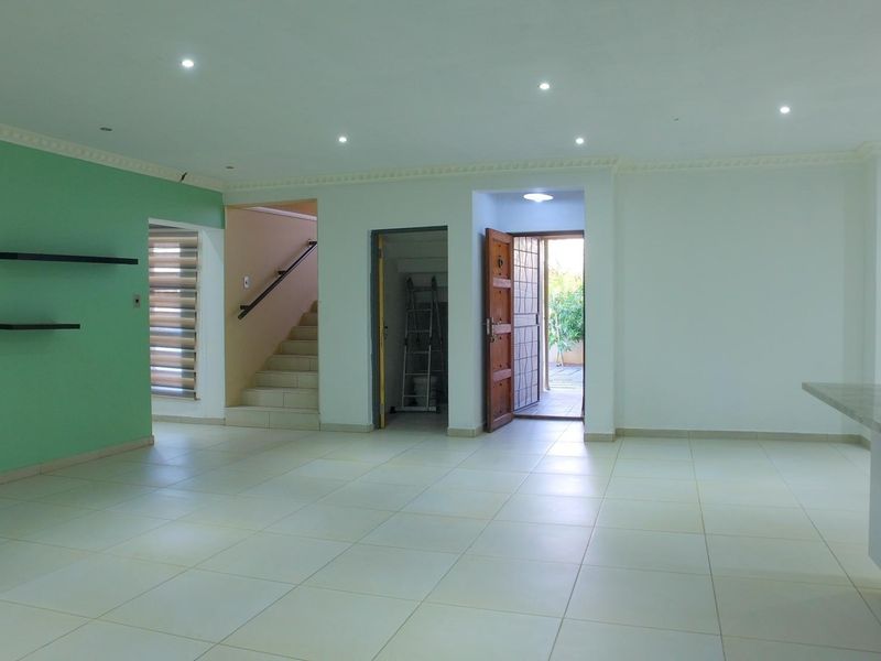 Spacious open-plan living area featuring tiled flooring, recessed lighting, and direct access to a staircase and exterior entrance.