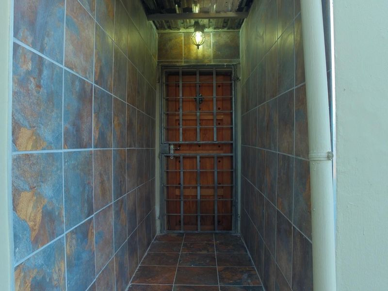 A narrow entrance passage featuring tiled walls and flooring, secured by a wooden door with an integrated metal security gate.