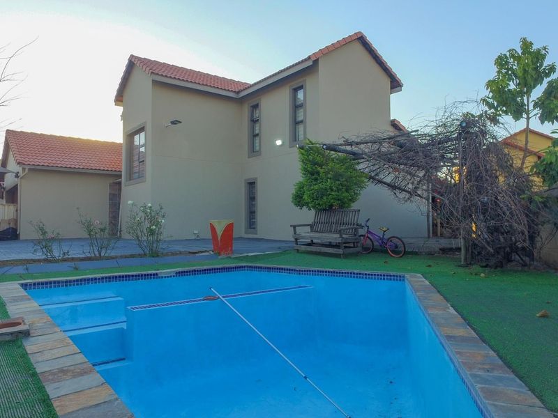 Rear exterior view featuring a swimming pool with tiled coping, paved patio area, and a two-story residential structure with terracotta roof tiles.