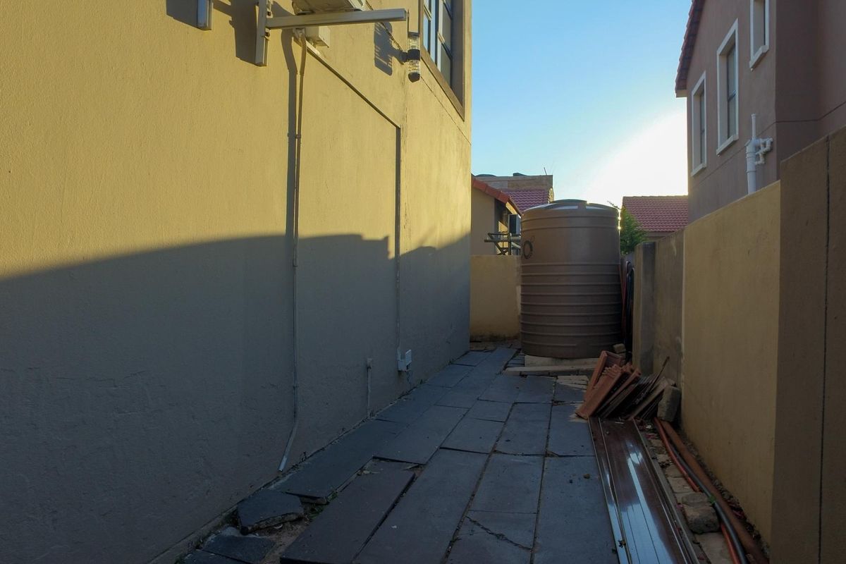 A side exterior walkway featuring a water storage tank, paved flooring, and boundary walling.