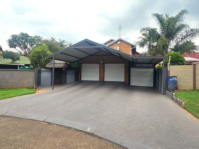 Front view of the property featuring a paved driveway, triple garage with a covered carport, and secure perimeter walling with electric fencing.