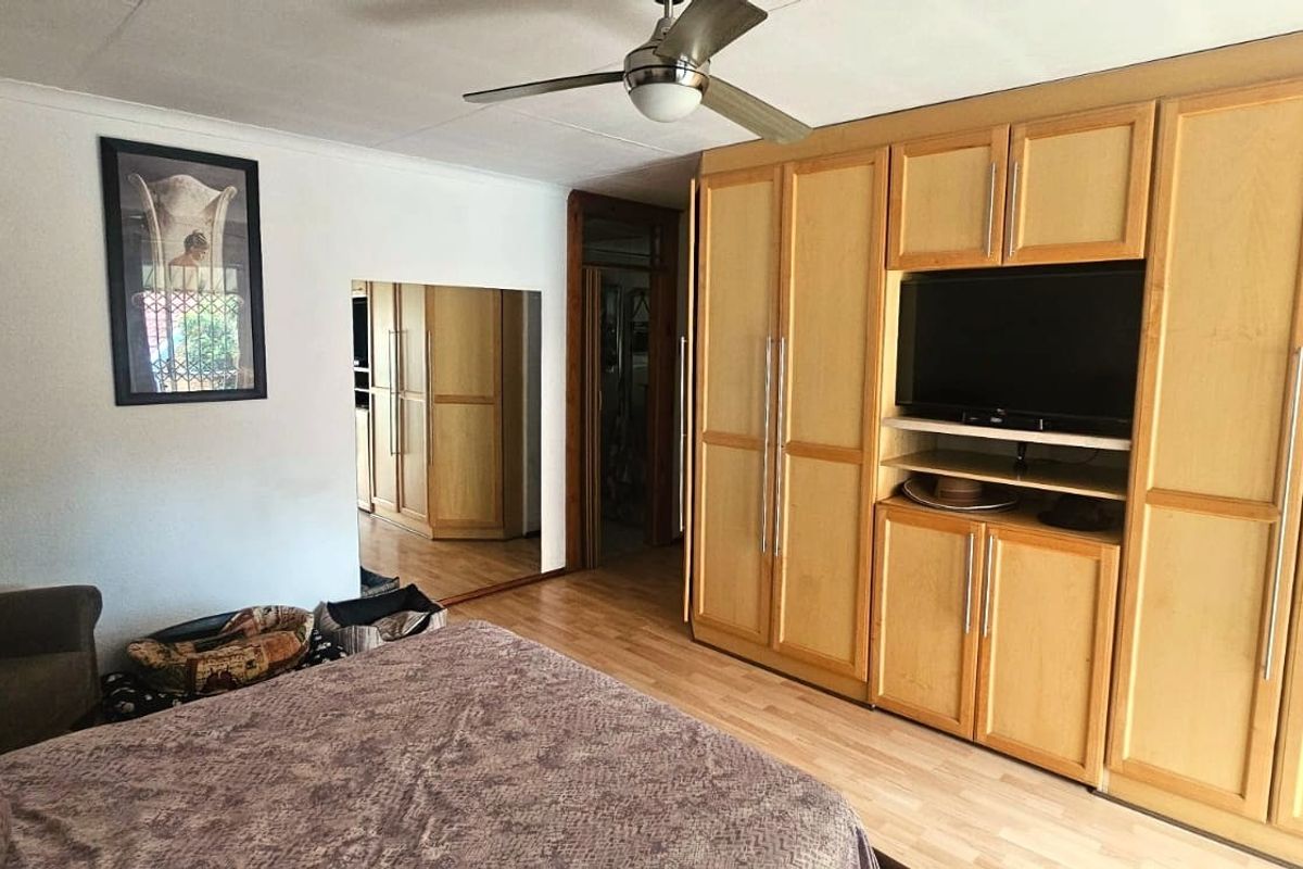 Bedroom featuring extensive built-in wooden cabinetry, laminate flooring, a ceiling fan, and a wall-mounted air conditioning unit.