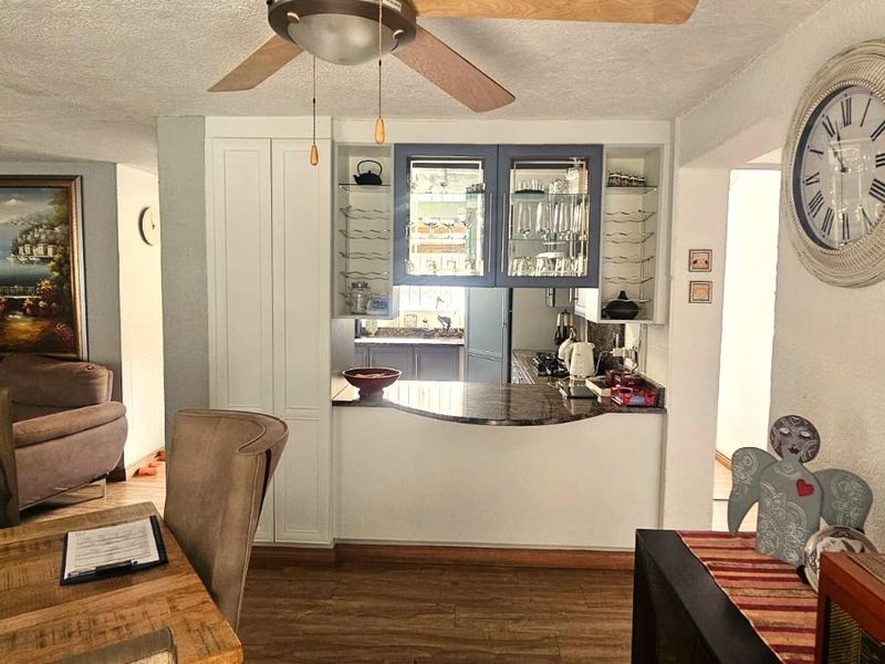Open plan living and dining area featuring a pass-through kitchen with built-in cabinetry, granite countertops, and a ceiling fan.