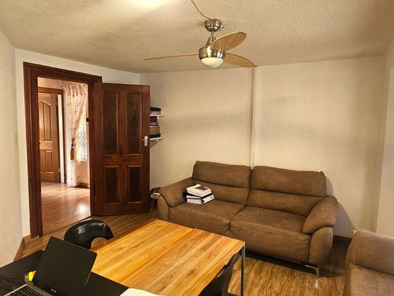 A living room featuring laminate flooring, a ceiling fan, and natural light through window blinds, providing a functional and comfortable living space.