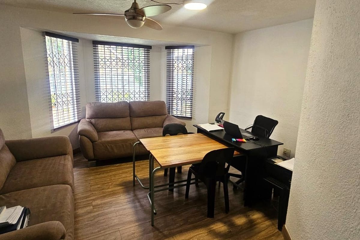 A living room area featuring laminate flooring, a ceiling fan, and a bay window with security bars.