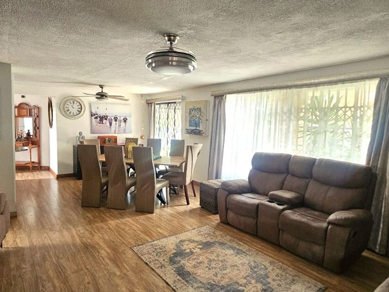 Spacious open-plan living and dining area featuring laminate flooring, a ceiling fan, and a wall-mounted air conditioning unit.