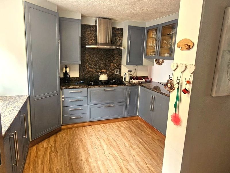 A functional kitchen featuring blue cabinetry, granite countertops, a stainless steel extractor fan, and a gas hob, with wood-look laminate flooring throughout.