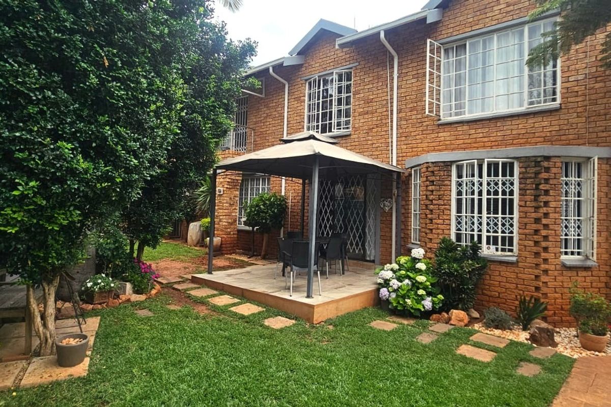 Rear view of a two-story brick house featuring a paved patio area, established garden, and security bars on the windows.