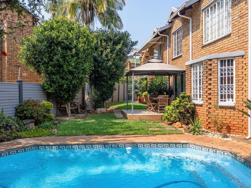 A private rear garden featuring a swimming pool, paved surround, and a brick-clad house exterior with security bars on the windows.