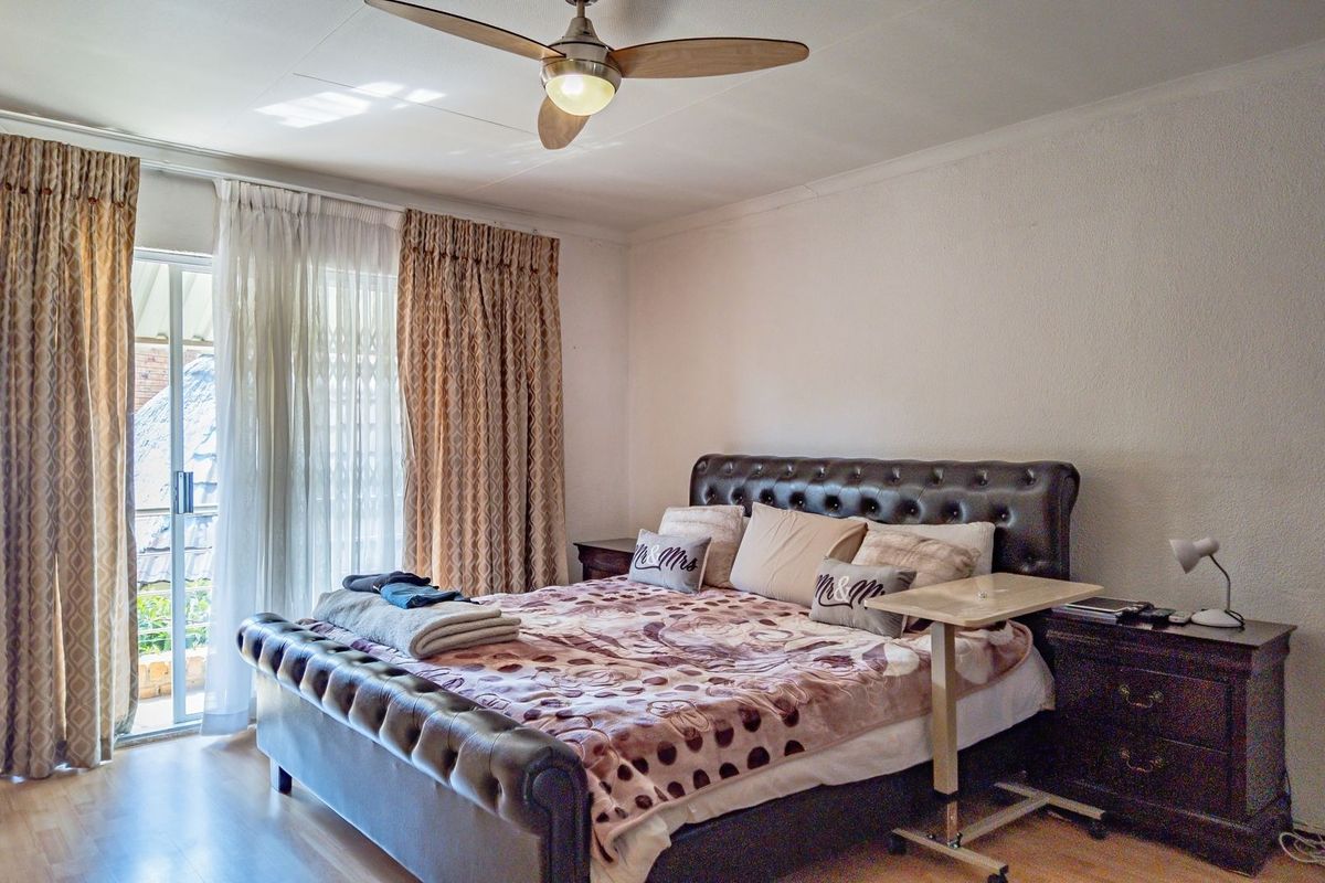 A well-lit bedroom featuring laminate flooring, a ceiling fan, and a sliding glass door providing access to the exterior.