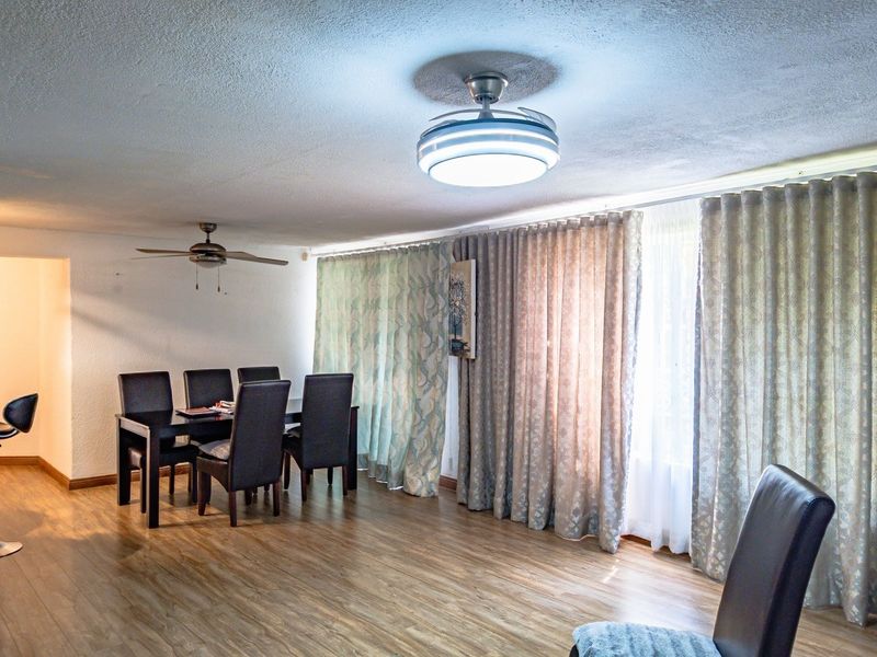 A dining area featuring laminate flooring, a ceiling fan, and large windows covered by floor-to-ceiling curtains.