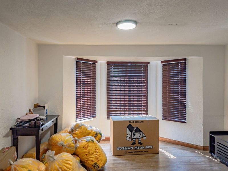 A living room featuring a bay window with venetian blinds, laminate flooring, and a central ceiling light fixture.