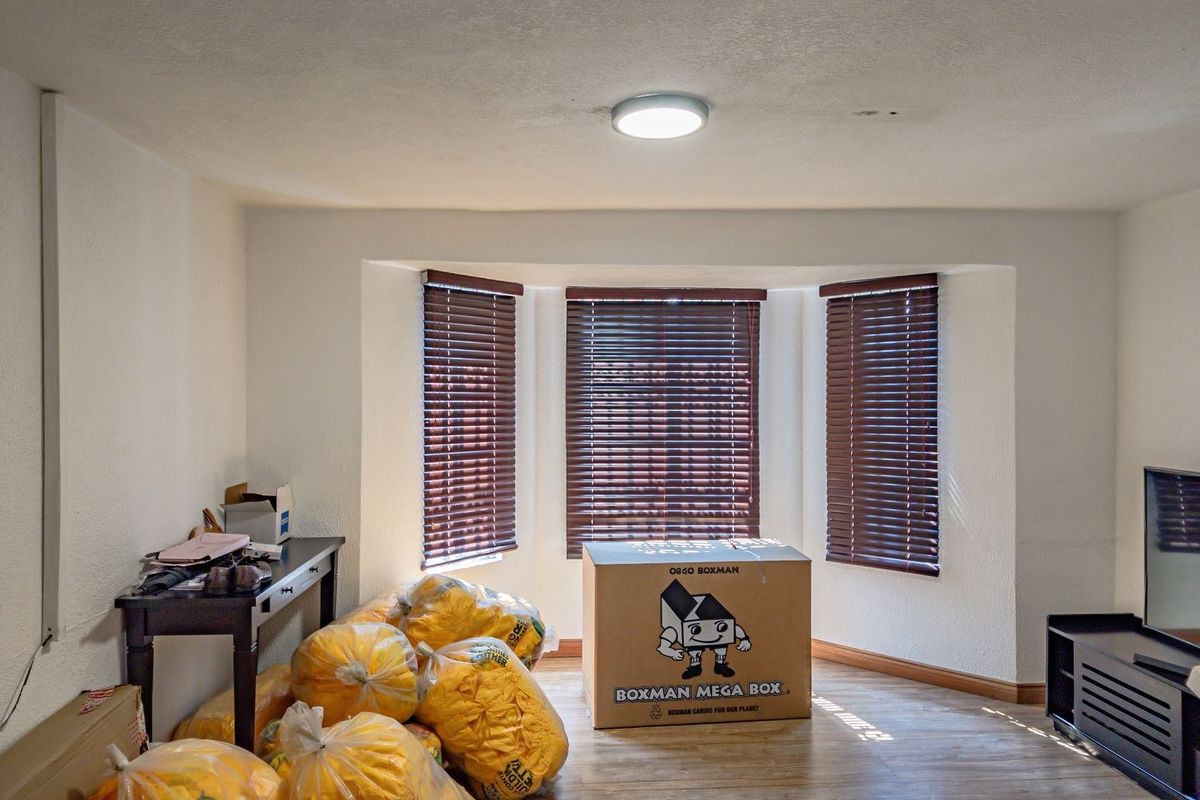 A living room featuring a bay window with venetian blinds, laminate flooring, and a central ceiling light fixture.