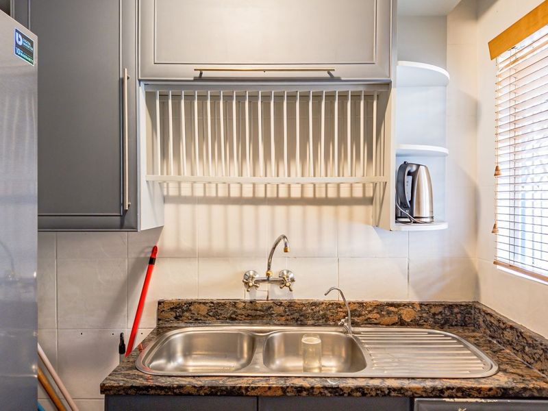 A functional scullery area featuring a double bowl stainless steel sink, granite countertops, and built-in cabinetry with an integrated dish drying rack.
