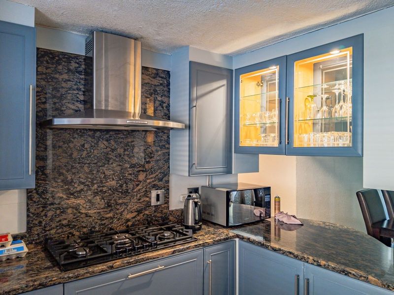 A well-appointed kitchen featuring blue cabinetry, granite countertops, a gas hob, and a stainless steel extractor fan with integrated display lighting.