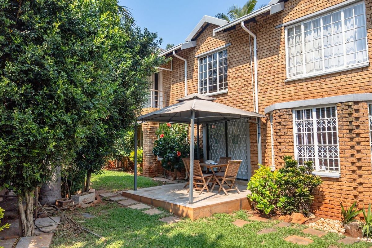 Rear view of the brick house featuring a paved patio area, established garden, and security bars on the windows.