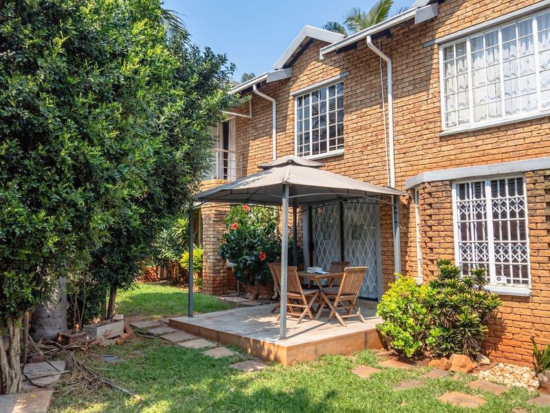 Rear view of the brick house featuring a paved patio area, established garden, and security bars on the windows.