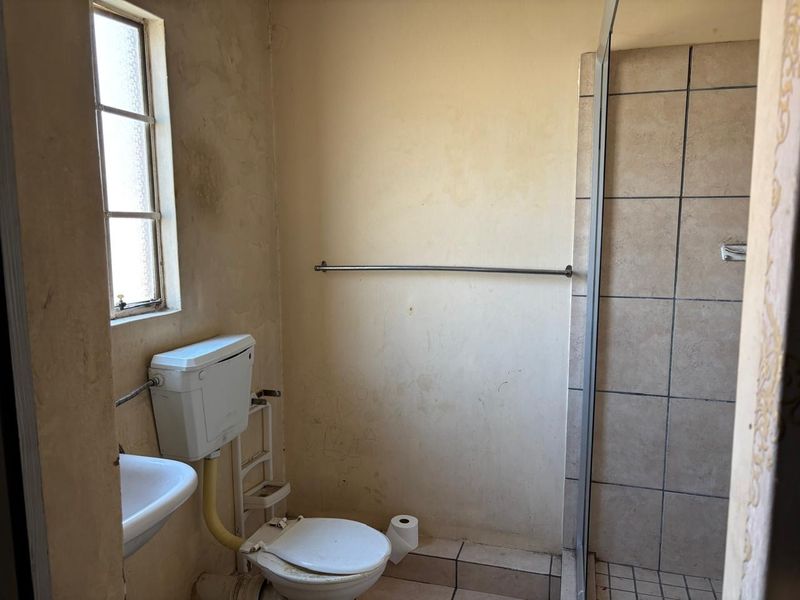 A dated bathroom featuring a shower enclosure, toilet, and wall-mounted basin, requiring significant cosmetic updates and surface repairs.