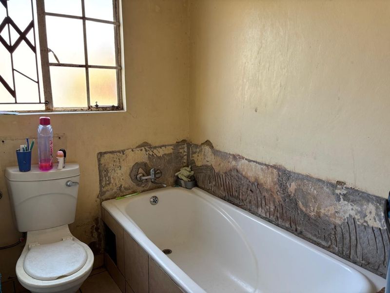 A bathroom featuring a bathtub and toilet, currently requiring significant wall repairs and retiling to restore the space.