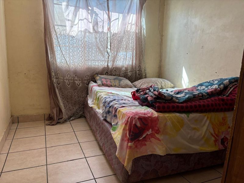 A bedroom featuring tiled flooring and a window, currently requiring cosmetic updates to the wall finishes to improve the overall condition.