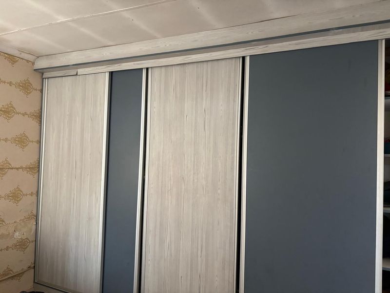 A bedroom featuring a large built-in sliding door wardrobe with a modern wood-grain and matte finish, requiring minor cosmetic repairs to surrounding walls and ceiling.