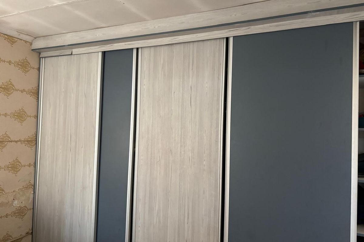 A bedroom featuring a large built-in sliding door wardrobe with a modern wood-grain and matte finish, requiring minor cosmetic repairs to surrounding walls and ceiling.