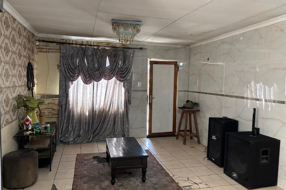 Living room featuring tiled flooring and wall cladding, requiring cosmetic updates and repairs to the ceiling and floor finishes.