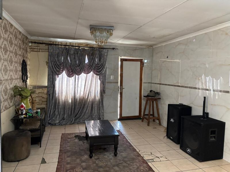 Living room featuring tiled flooring and wall cladding, requiring cosmetic updates and repairs to the ceiling and floor finishes.